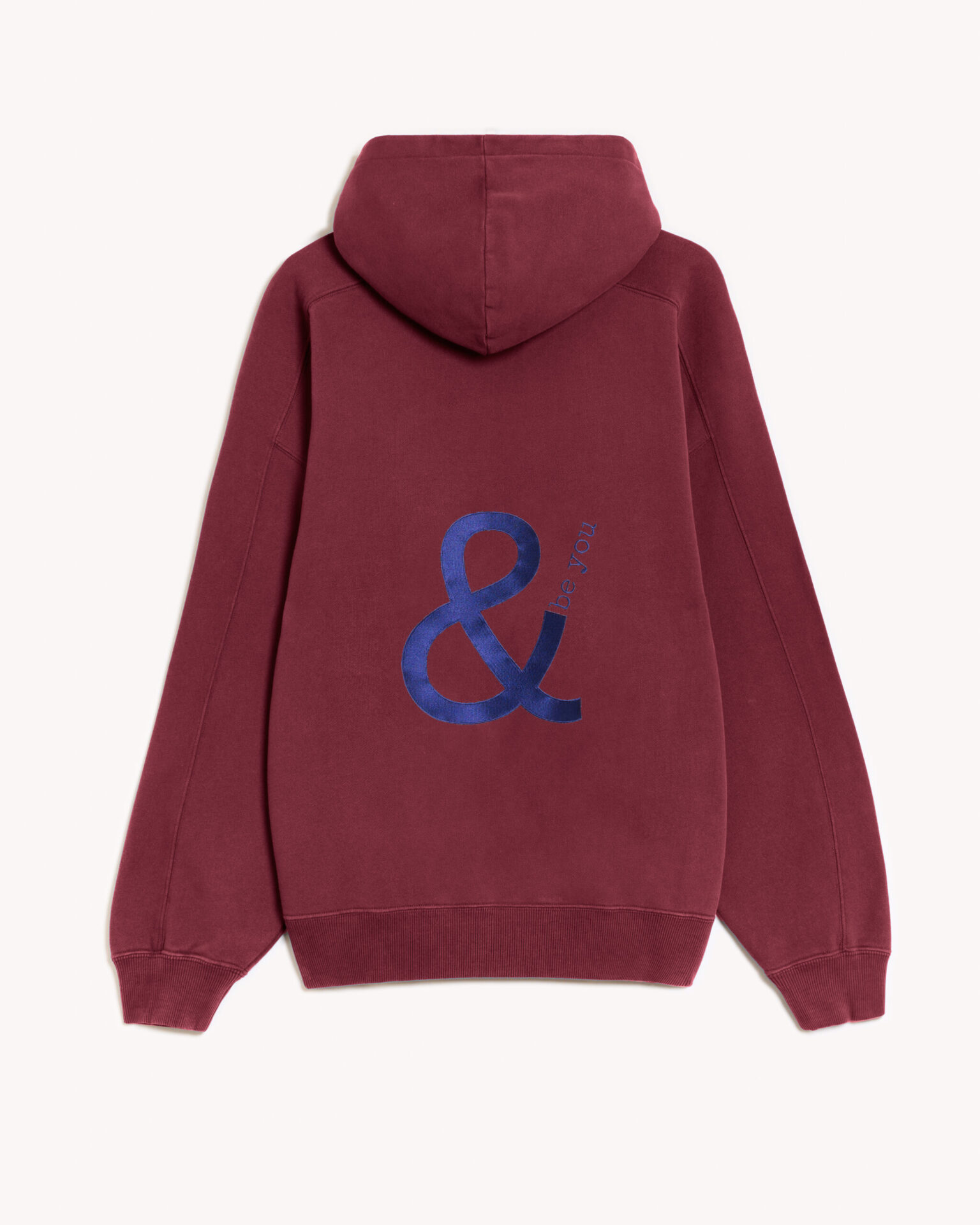 Imagen de la parte trasera de la hoodie modelo Cistierna con capucha en color granate con el logo de and be you brand bordado en color azul marino. Modelo unisex de corte holgado y hombro caído.